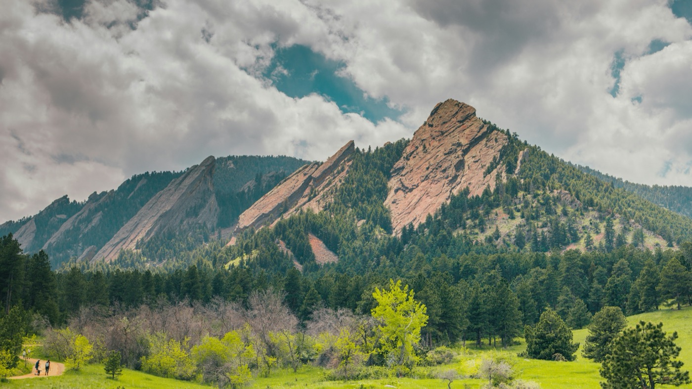 Boulder Flatirons from Chautauqua Park with green spring meadow and hikers on the trail