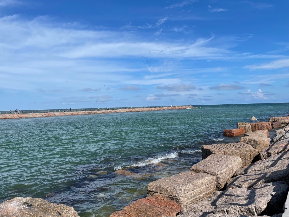 Stone jetty extending into turquoise Gulf of Mexico waters under blue sky, Corpus Christi Texas