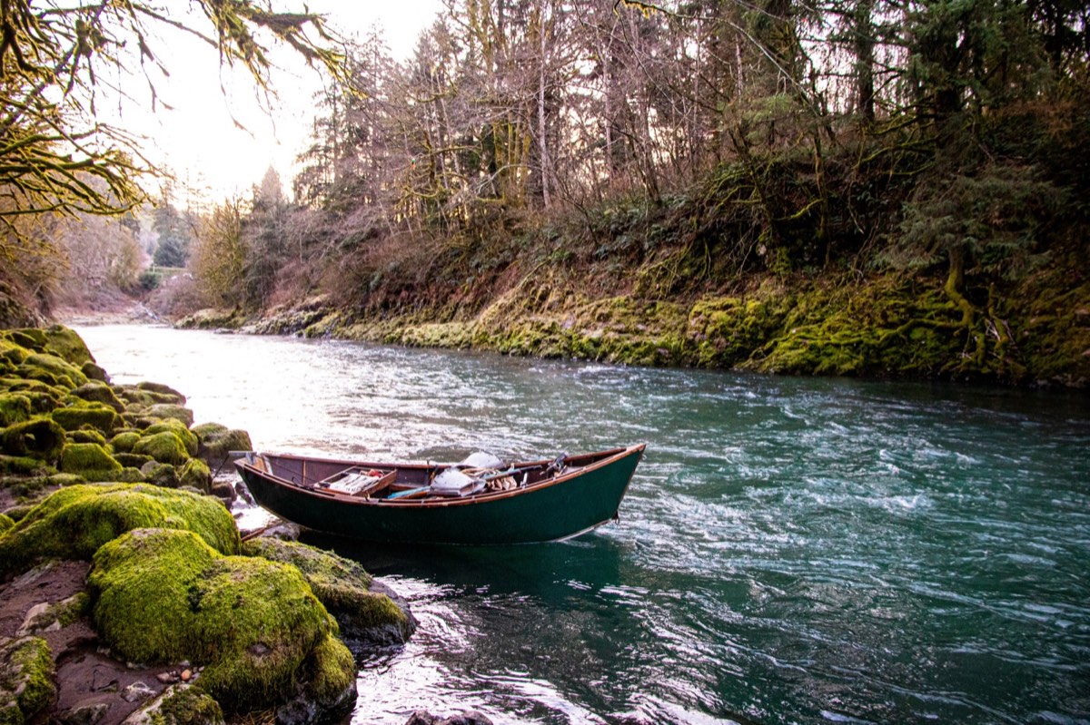 Wooden drift boat on a scenic Oregon river with moss-covered rocks and forest