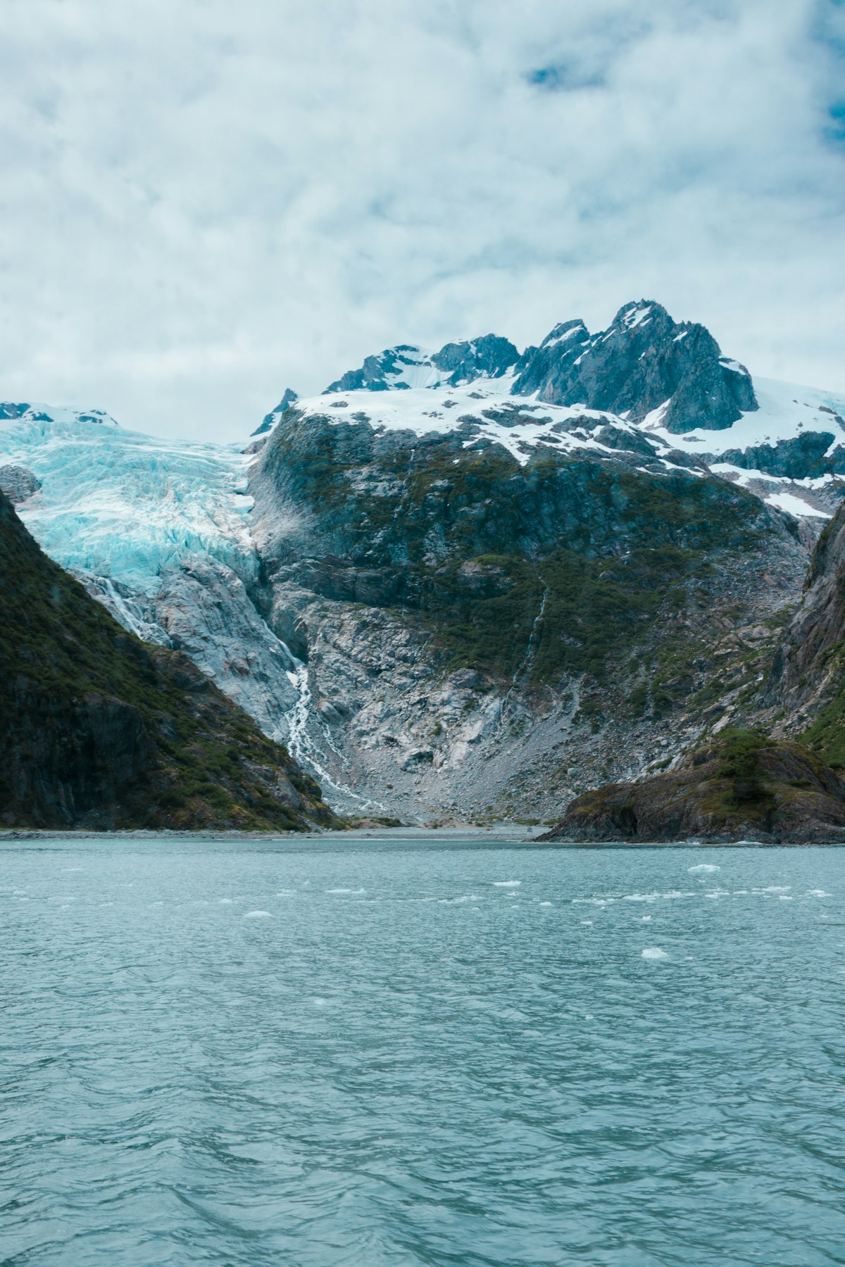 A glacier sitting beside snow-capped mountains at Kenai Fjords, Alaska