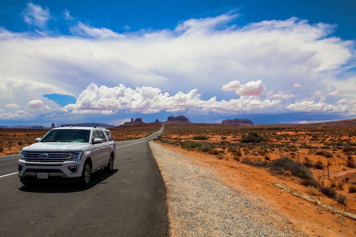 White SUV driving down a desert road in Monument Valley, USA