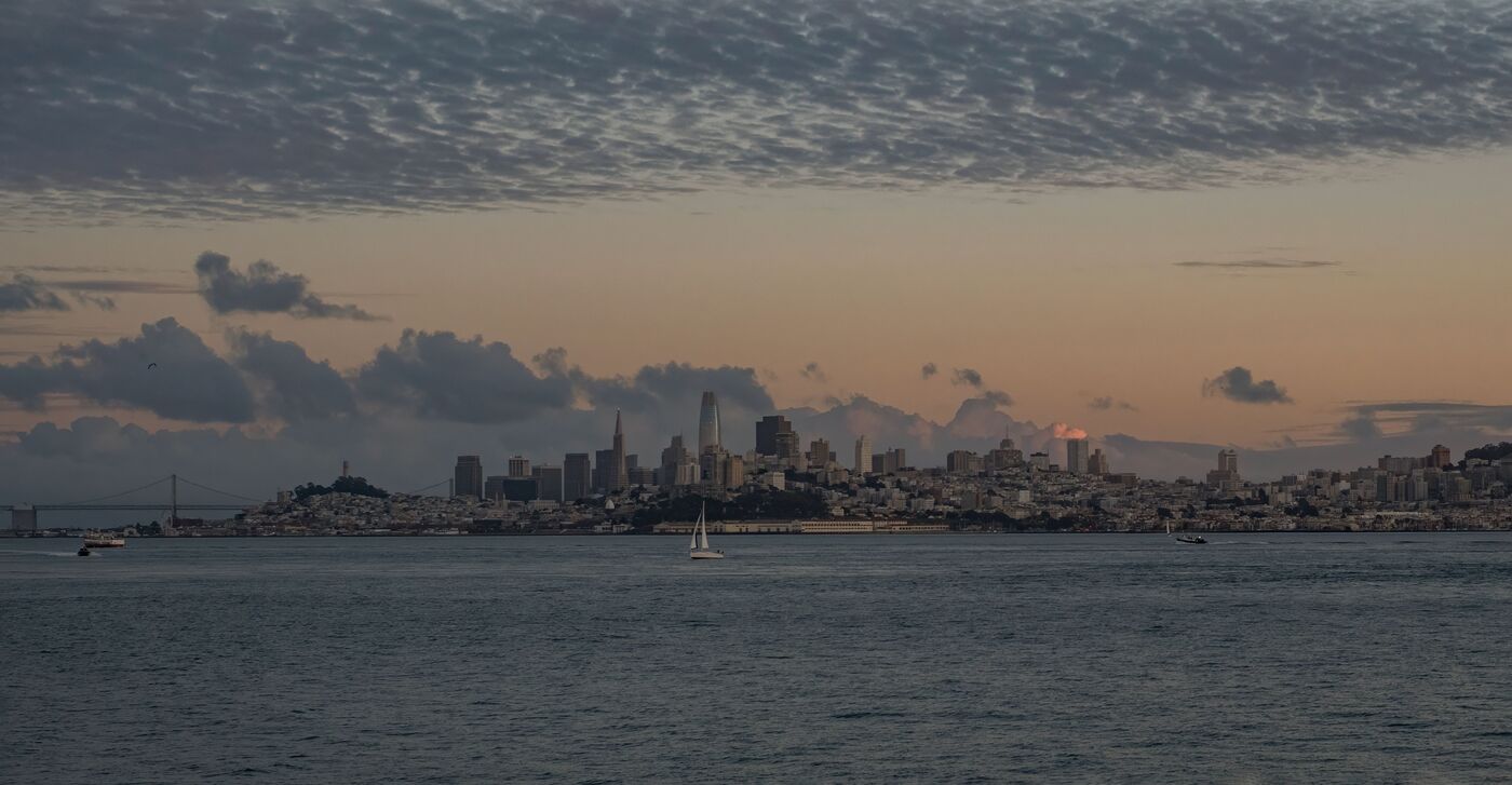 San Francisco city skyline with the Bay Bridge and a sailboat in the foreground at dusk, California