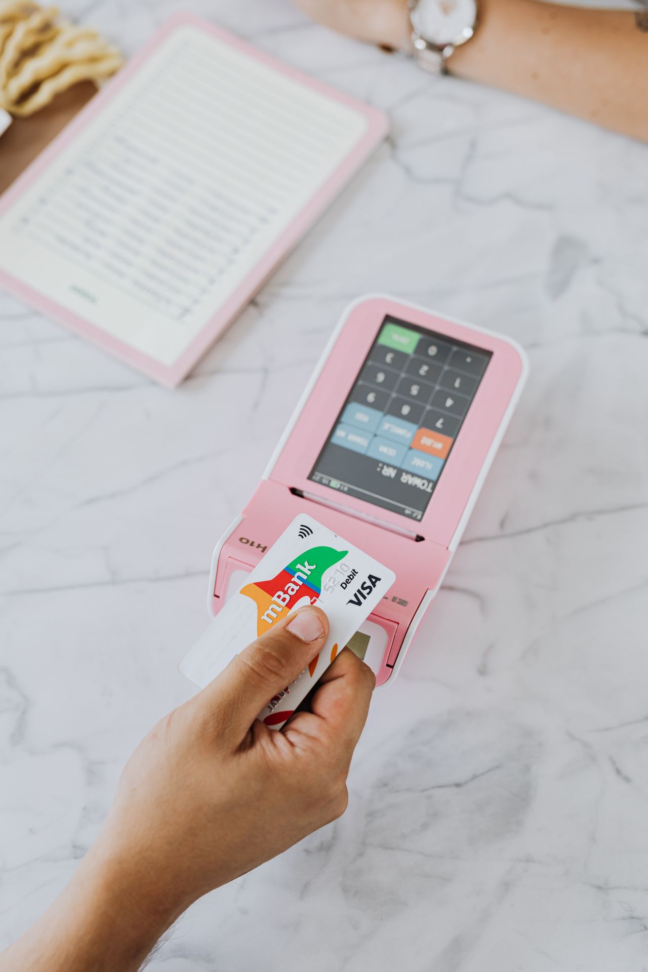 Hand inserting a Visa card into a pink POS payment terminal