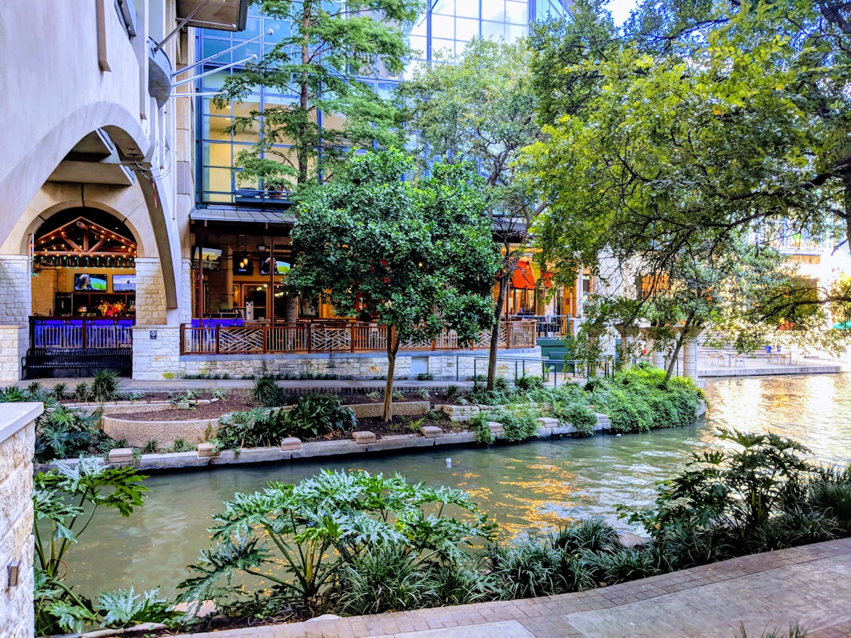 The San Antonio River Walk with a tall hotel tower rising above the tree-lined canal, Texas